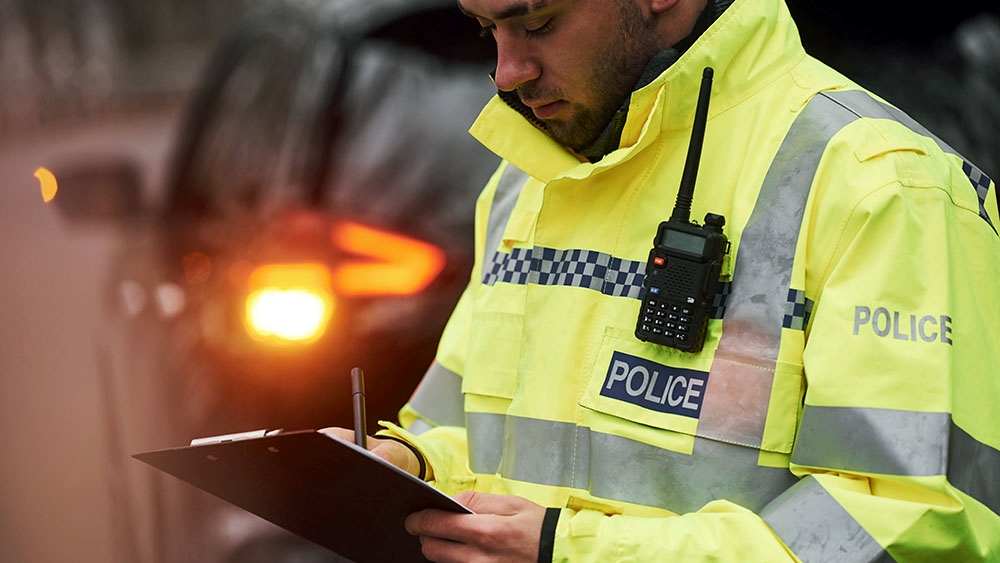 Male Police Officer In Green Uniform Standing With Notepad Near Car Male Police Officer In Green Uniform Standing With Notepad Near Car