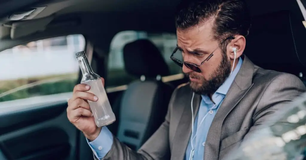 Man in a suit sitting in a car holding a bottle, illustrating potential DUI scenarios and legal implications in Florida.