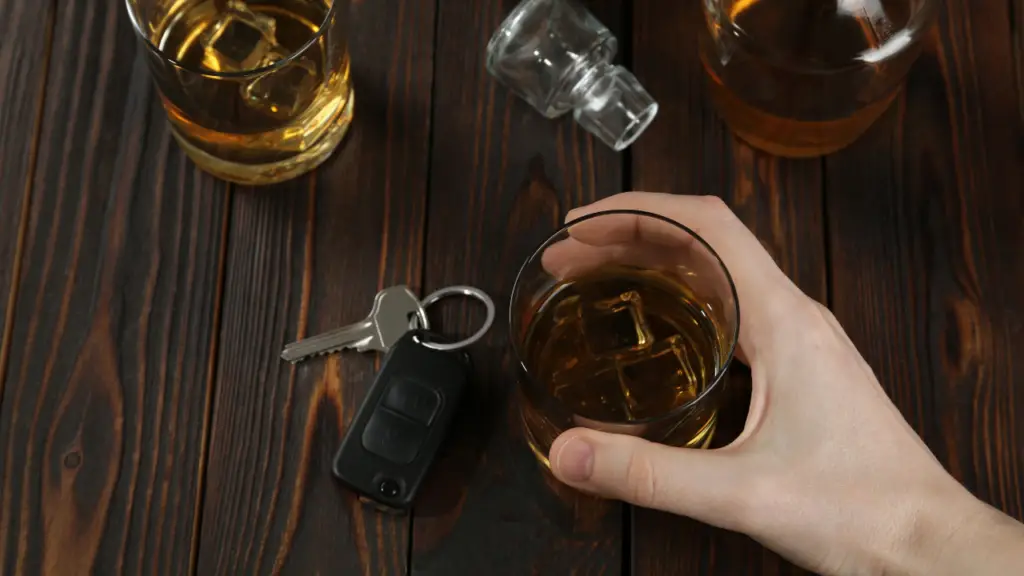 Hand holding a glass of whiskey with ice, car keys nearby, and additional whiskey glasses in the background, illustrating the risks associated with DUI in Florida.