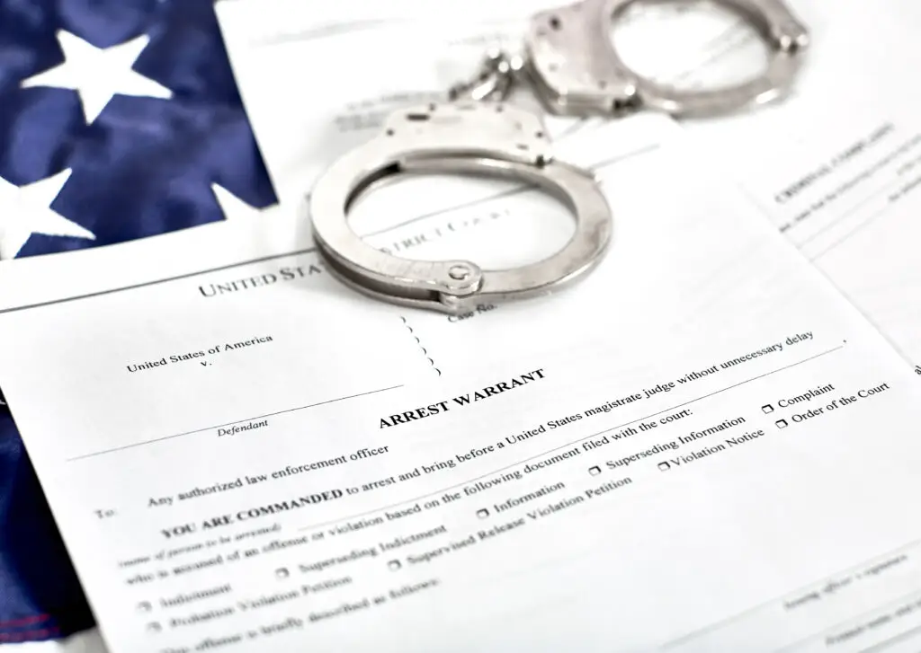 Arrest warrant document with handcuffs on a background featuring an American flag, relevant to legal risks associated with active warrants at the DMV in Florida.