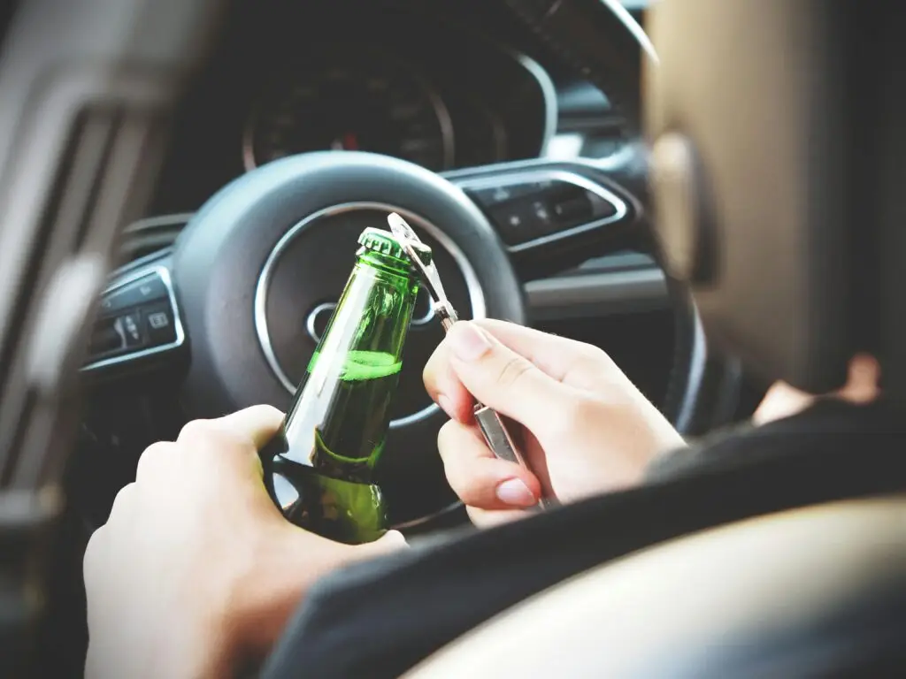 Person opening a green beer bottle inside a car, highlighting risky behavior related to DUI.