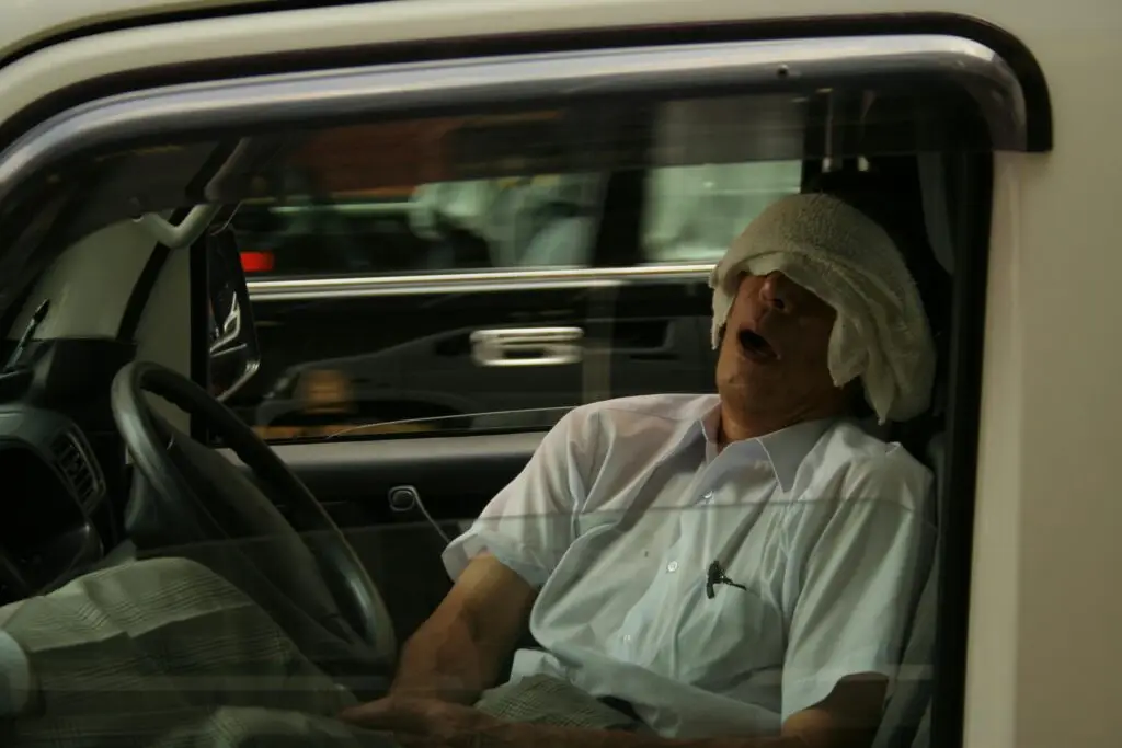 Man sitting in a parked car with a towel over his eyes, appearing to be asleep, illustrating the concept of “actual physical control” related to DUI laws in Florida.