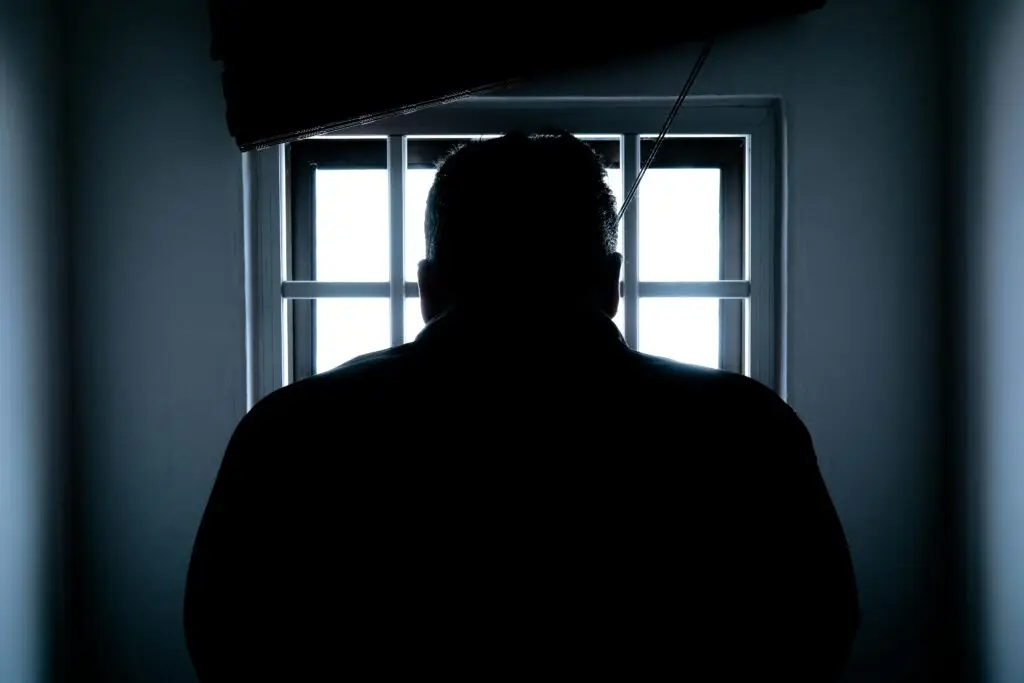 Silhouette of a person facing a barred window, symbolizing the consequences of criminal charges and the importance of hiring a criminal attorney in Florida.