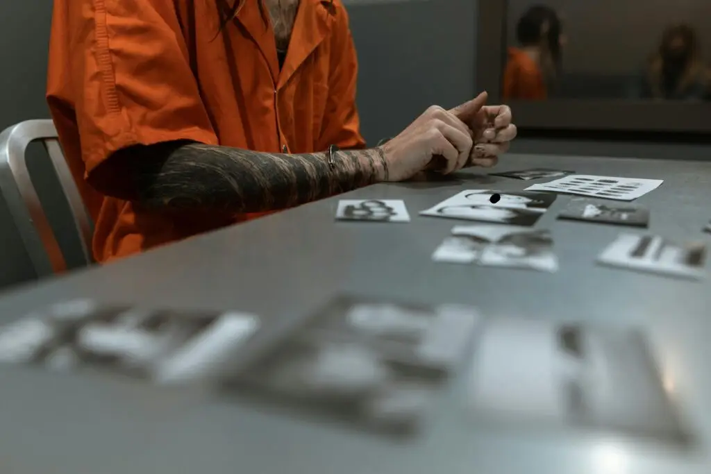 Person in orange prison jumpsuit examining photographs on a table, reflecting serious legal implications related to accusations of sex crimes involving children in Florida.