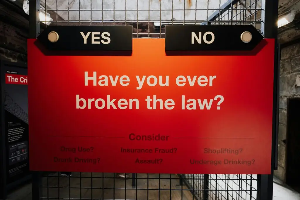 Sign asking "Have you ever broken the law?" with options "YES" and "NO," and examples of offenses like drug use, drunk driving, insurance fraud, assault, shoplifting, and underage drinking.