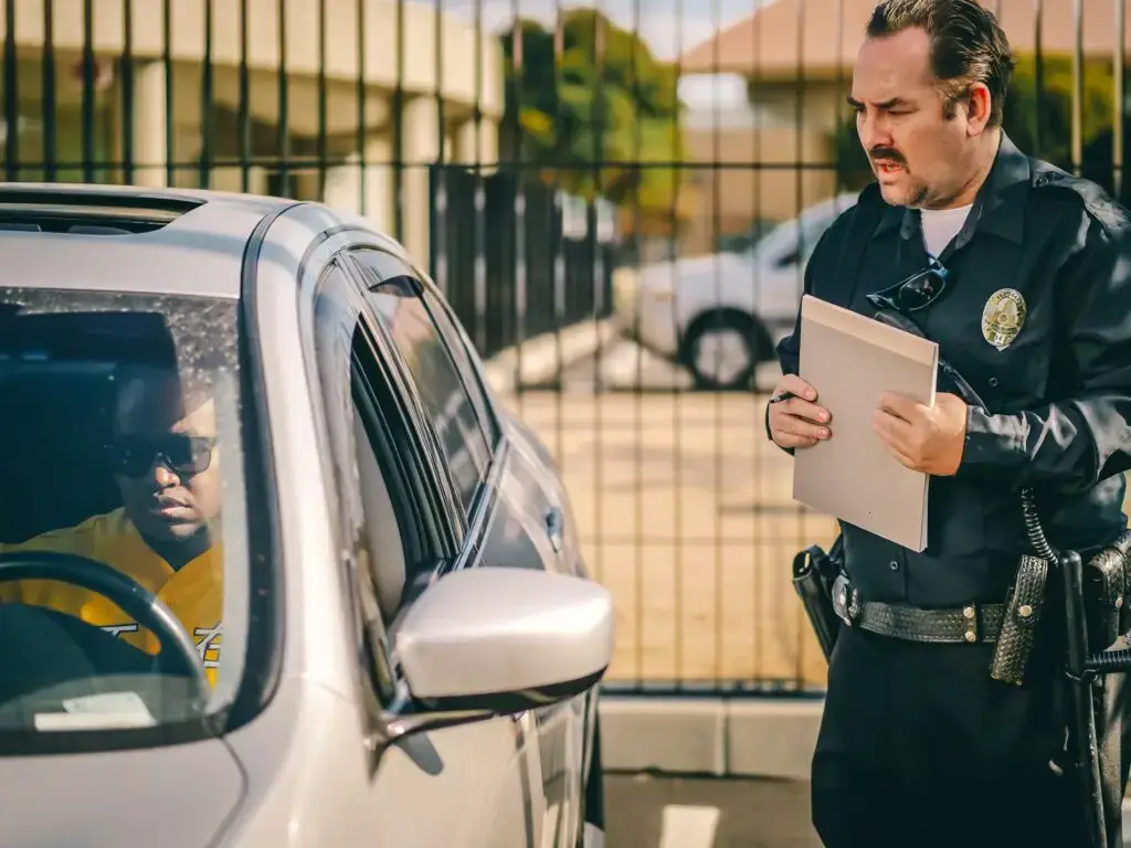 Driver with sunglasses in a car interacting with a police officer holding a clipboard, illustrating a traffic stop related to driving without a valid license in Florida.