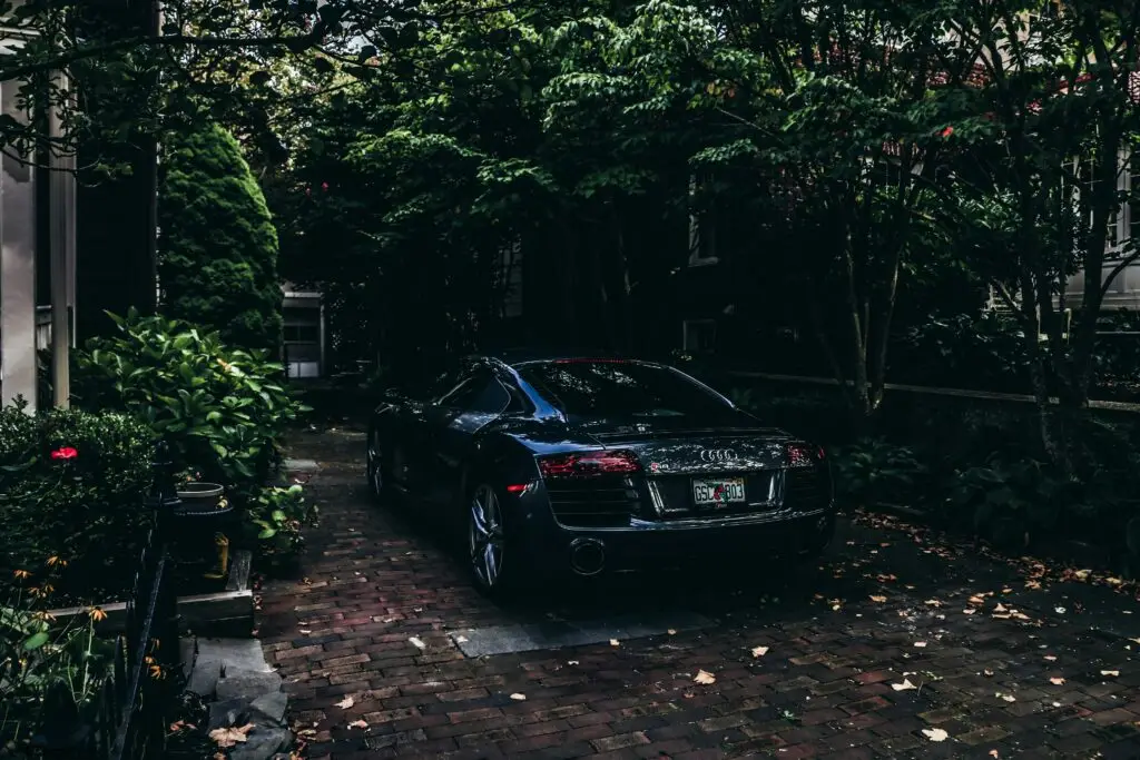 Black Audi sports car parked in a lush, green driveway, surrounded by trees and foliage, emphasizing the potential legal implications of driving with an expired tag in Fort Lauderdale.