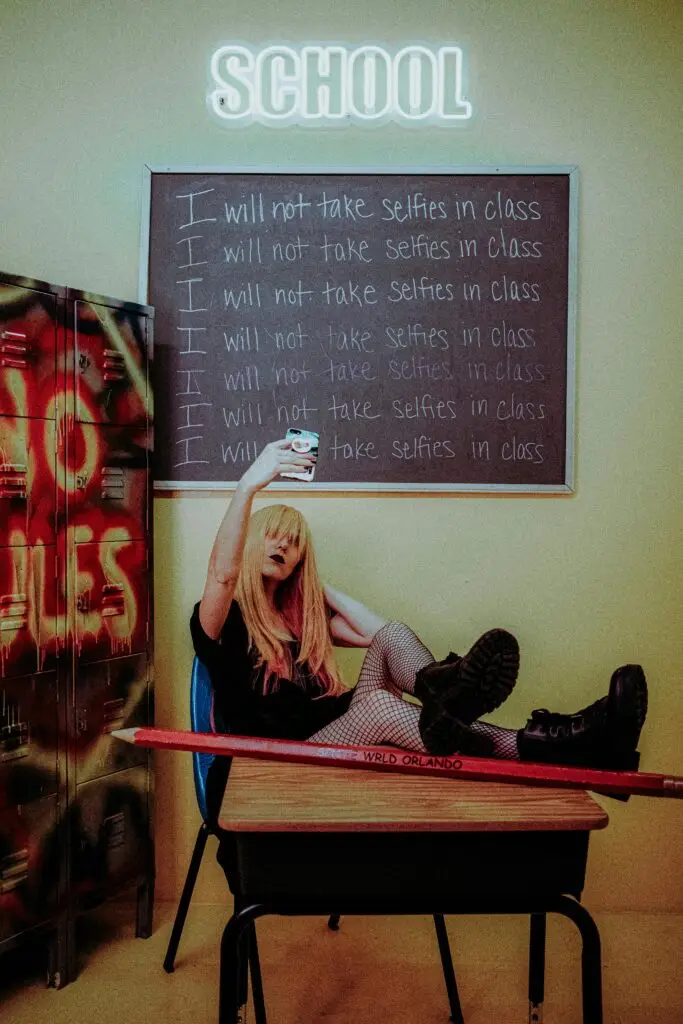 Teen girl taking a selfie in a classroom with “I will not take selfies in class” written on the chalkboard — school discipline concept -- representing expunging a juvenile record in Florida