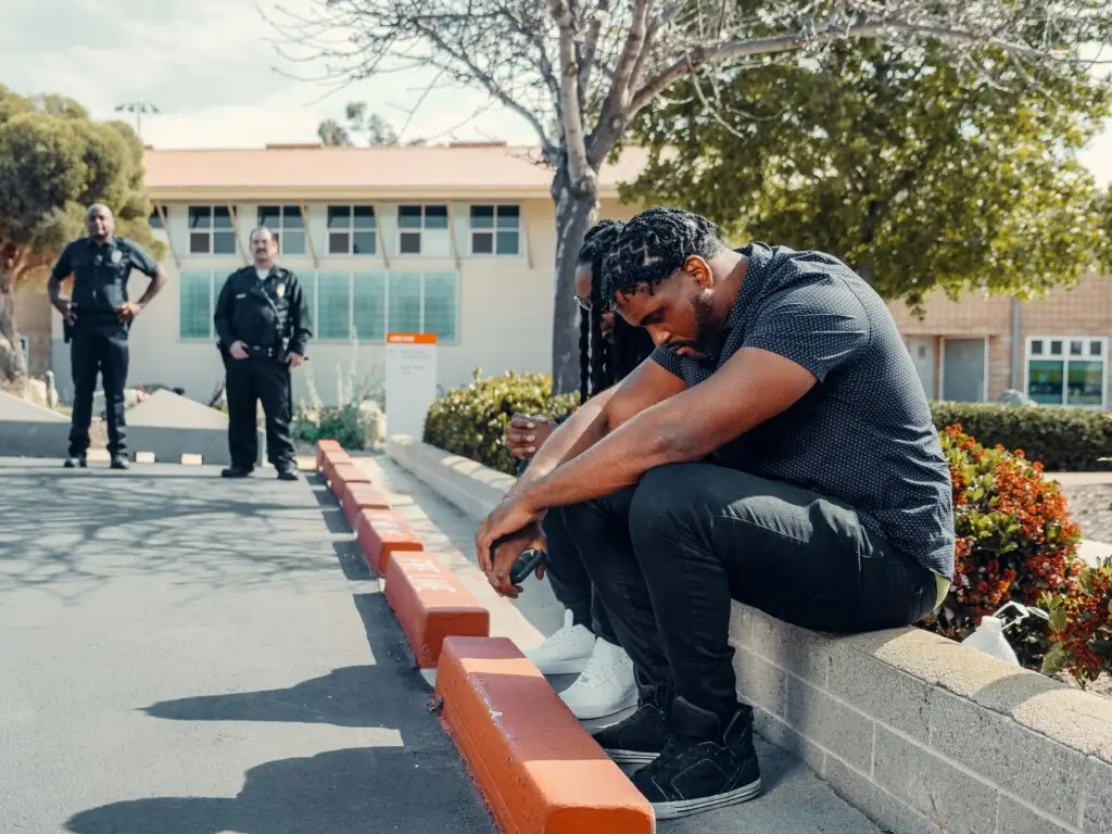 Man arrested for 3rd degree grand theft in Florida sitting on curb with police officers in background