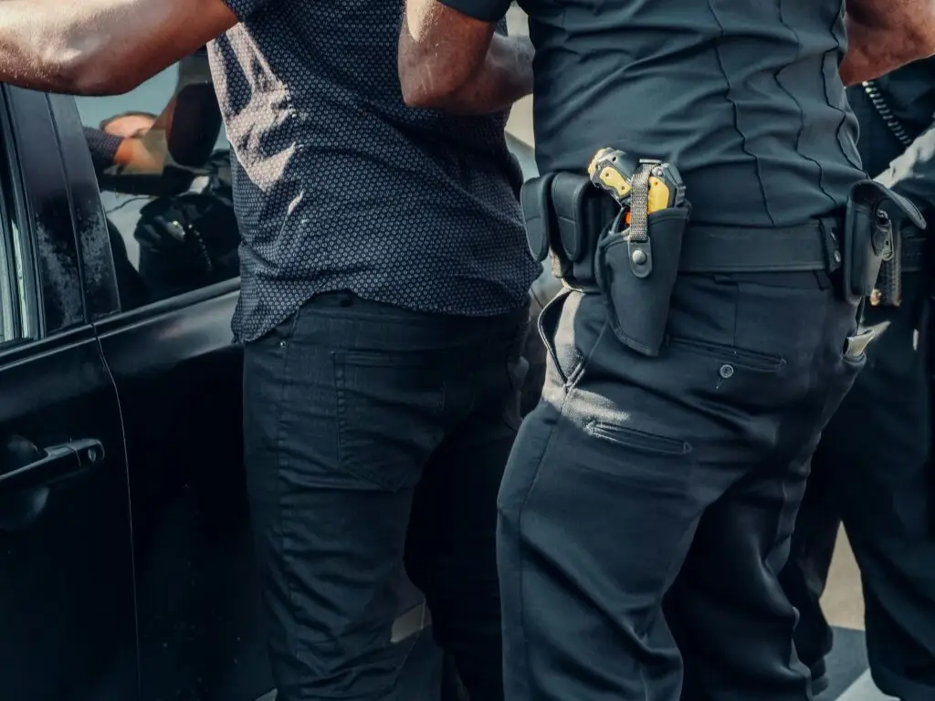 A man is detained by police next to a vehicle, symbolizing an arrest for theft in Fort Lauderdale.