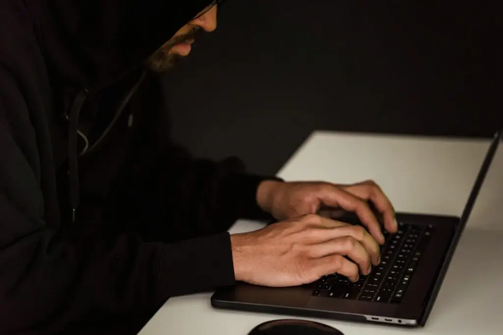 A man in a dark hoodie typing on a laptop, representing cyber fraud or internet-based financial crimes in Florida.