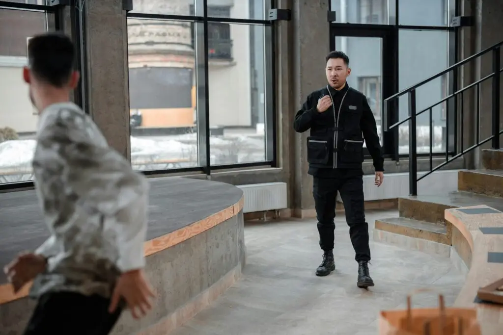 Man in a black vest and pants standing in an industrial space, confronting another person running away, emphasizing themes of theft and legal consequences related to grand theft charges in Florida.